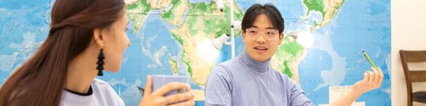 Male student speaking to female student holding a cup sitting in a classroom.